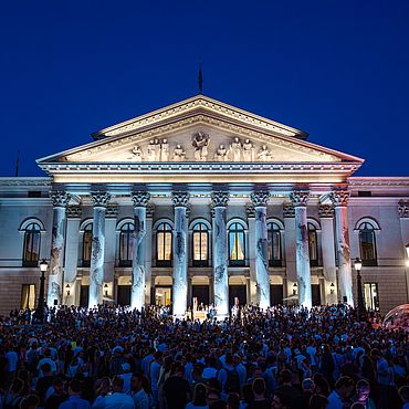 Das Nationaltheater beleuchtet bei Nacht eine Masse an Menschen feiert davor